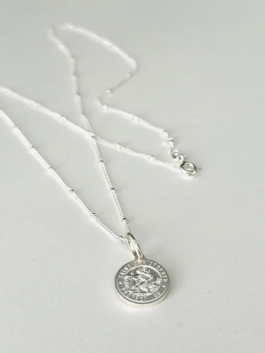 Silver necklace with a round pendant on a light gray background